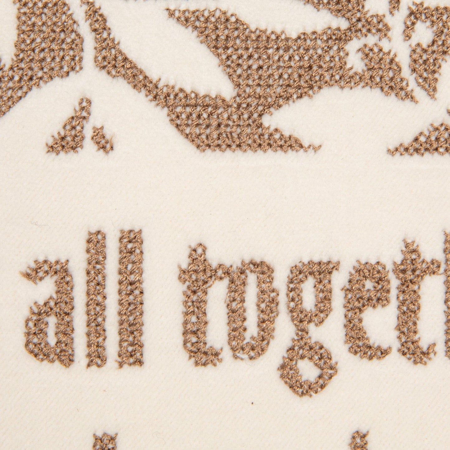 Close-up of cream velvet pillow with brown embroidered text reading 'all together' and decorative motifs