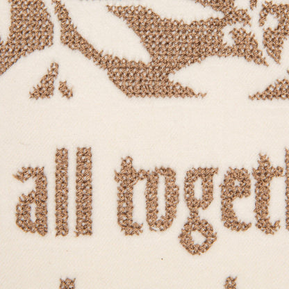 Close-up of cream velvet pillow with brown embroidered text reading 'all together' and decorative motifs