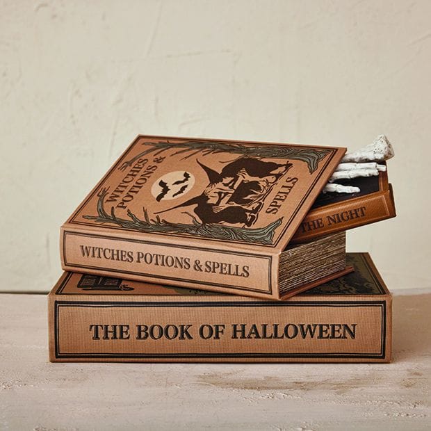 Stack of three Halloween-themed book-shaped storage boxes with spooky decorative covers and skeleton hand detail