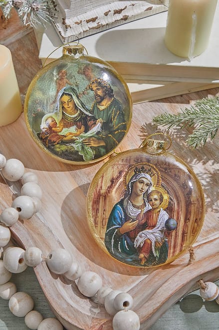 Two round glass disc ornaments featuring religious nativity scenes with gold trim, lifestyle display