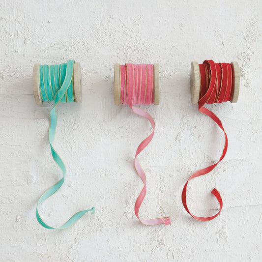 Three wood spools of velvet ribbon in teal, pink, and red with gold edges